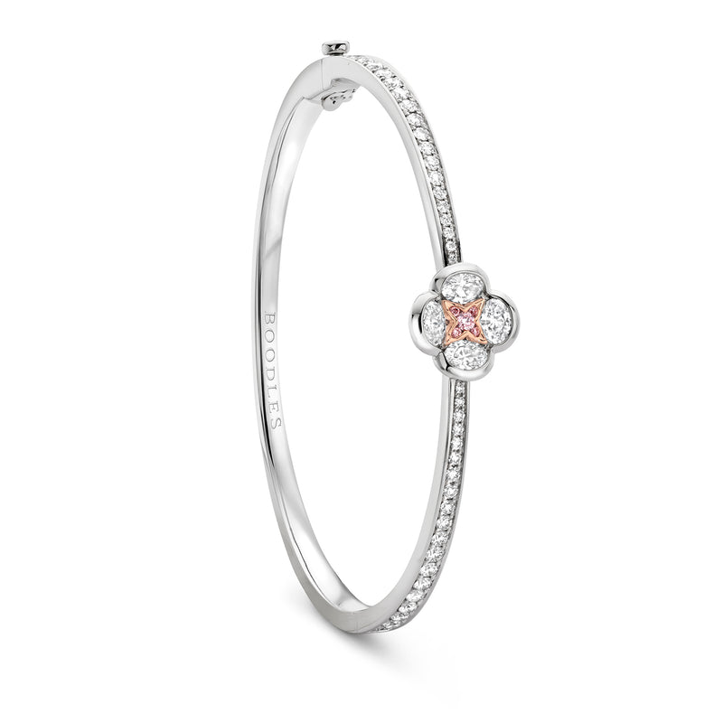 A silver-toned hinged bangle bracelet featuring a small flower-shaped cluster with a central peach-pink gemstone surrounded by clear stones, shown on a plain white background.