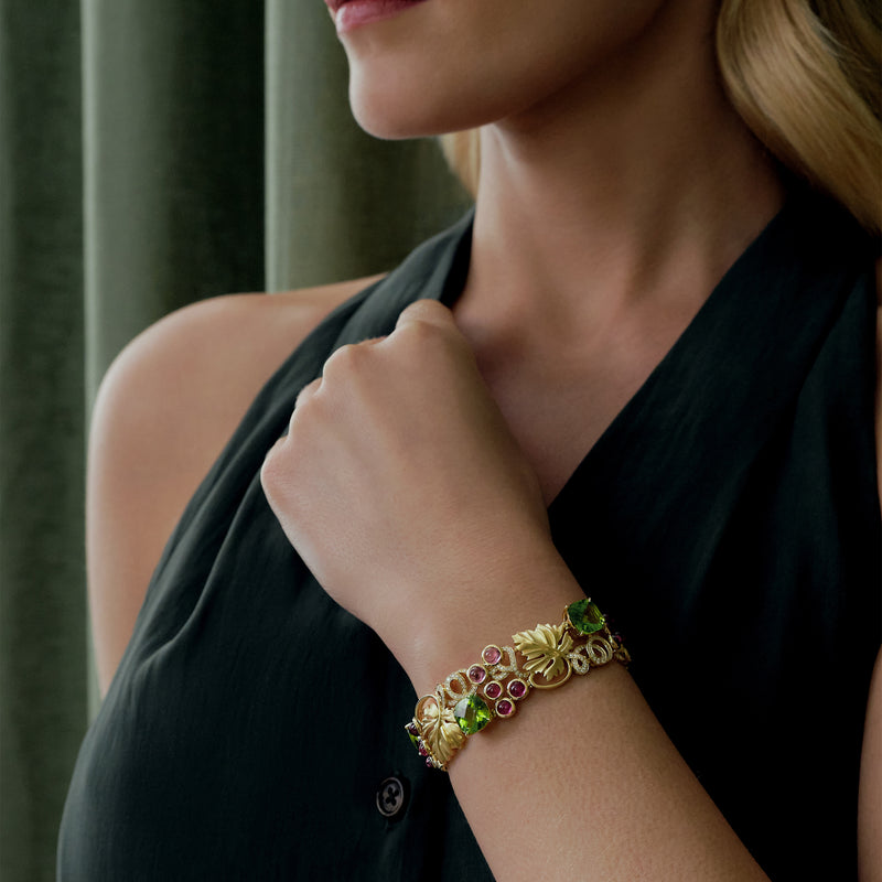 Woman wearing a gold bracelet with green and red stones against a neutral background