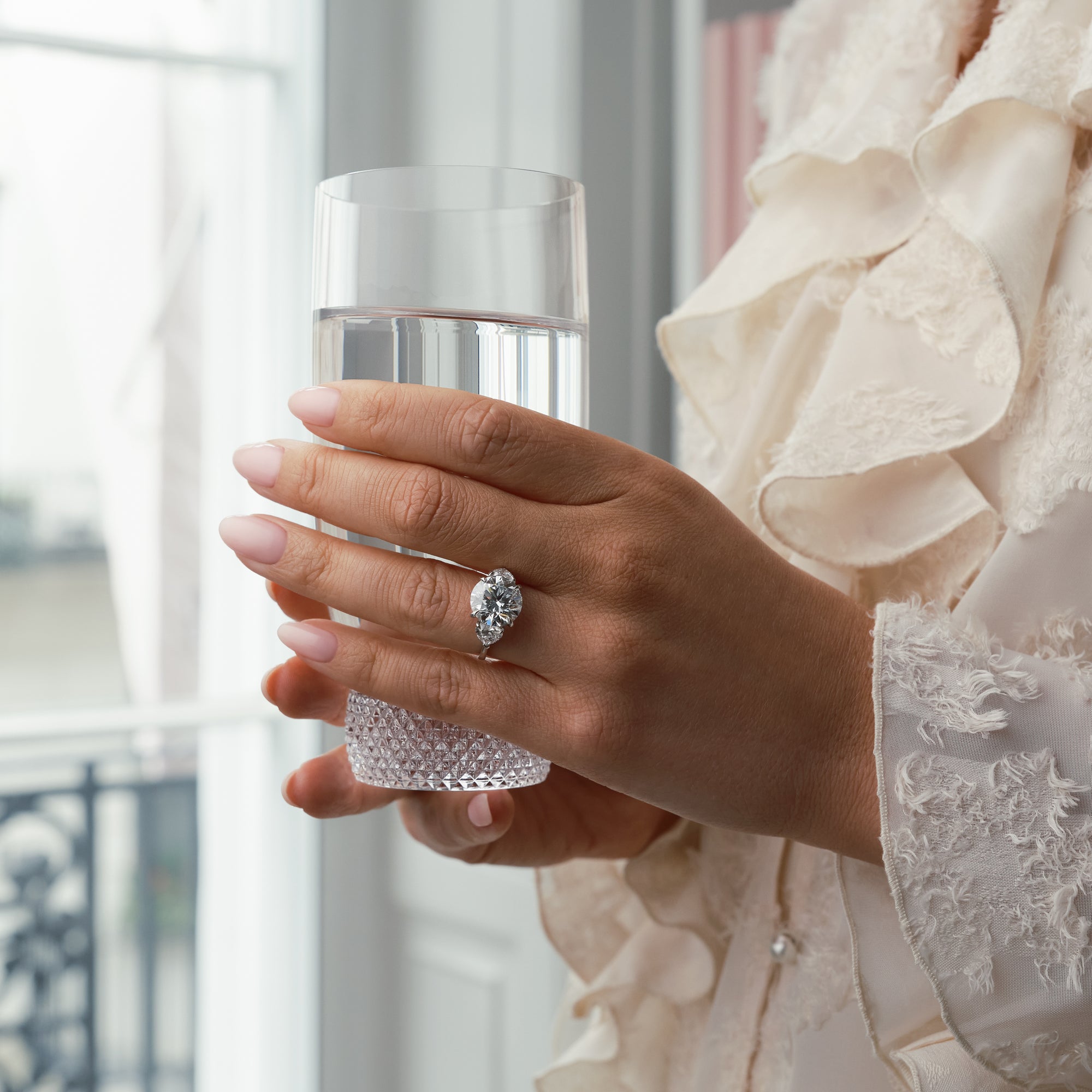 Petal diamond and platinum engagement ring worn by a woman holding a glass of water.