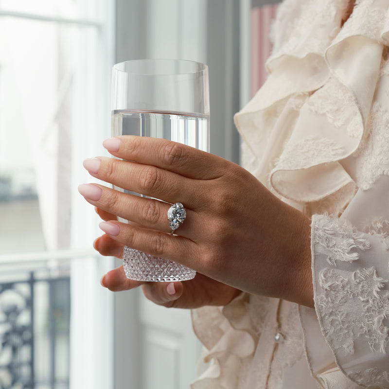 Petal diamond and platinum engagement ring worn by a woman holding a glass of water.