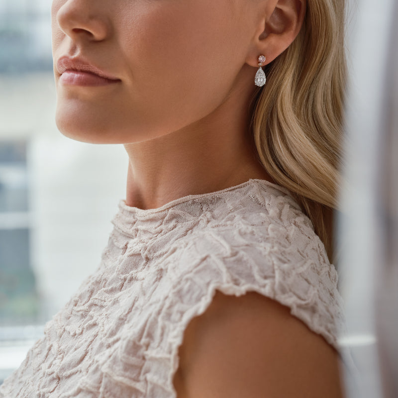 Classic brilliant pink diamond and pear diamond drop earrings worn by a woman.