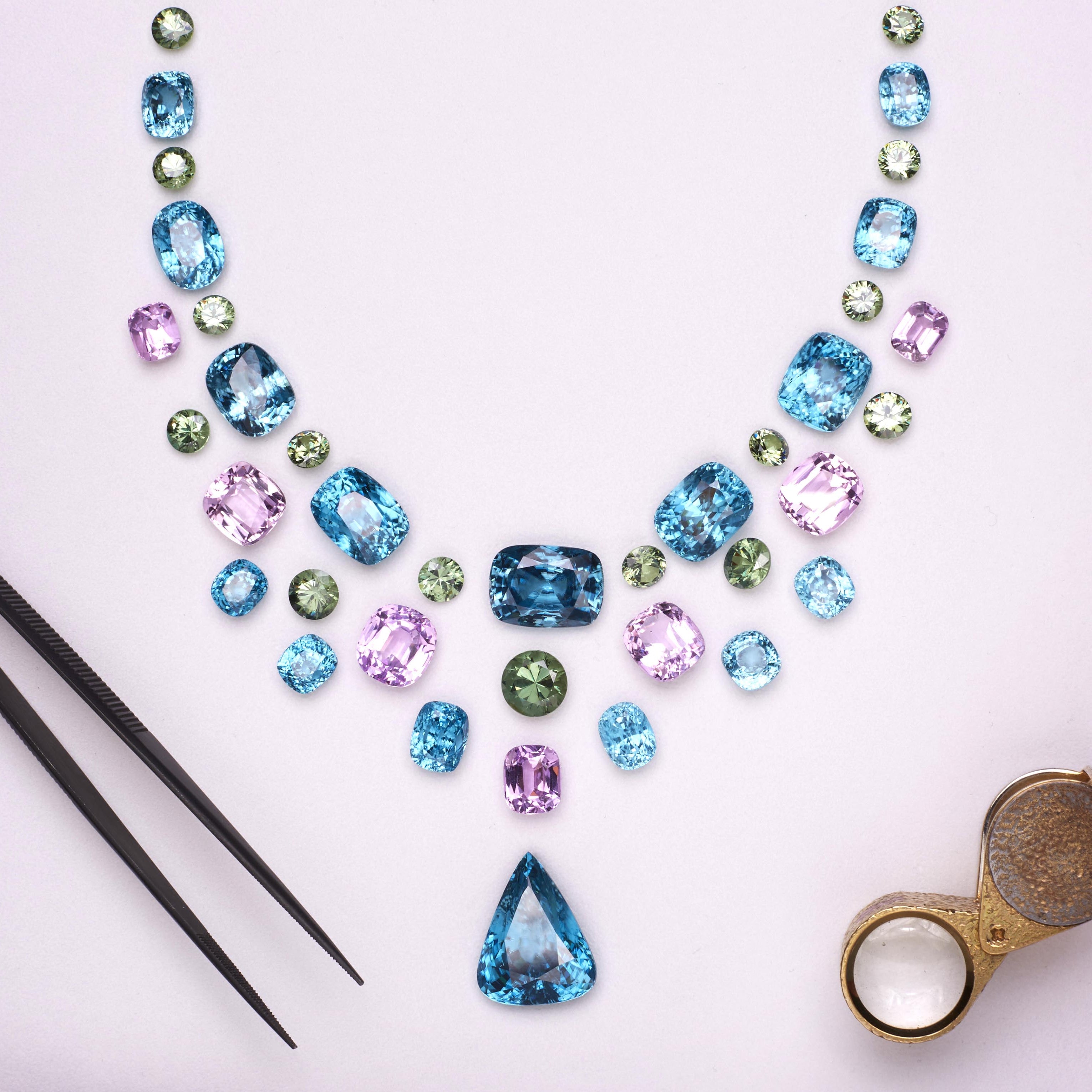 A colorful gemstone necklace displayed on a white card, surrounded by tweezers, a magnifying lens, and a pink booklet labeled Boodles.