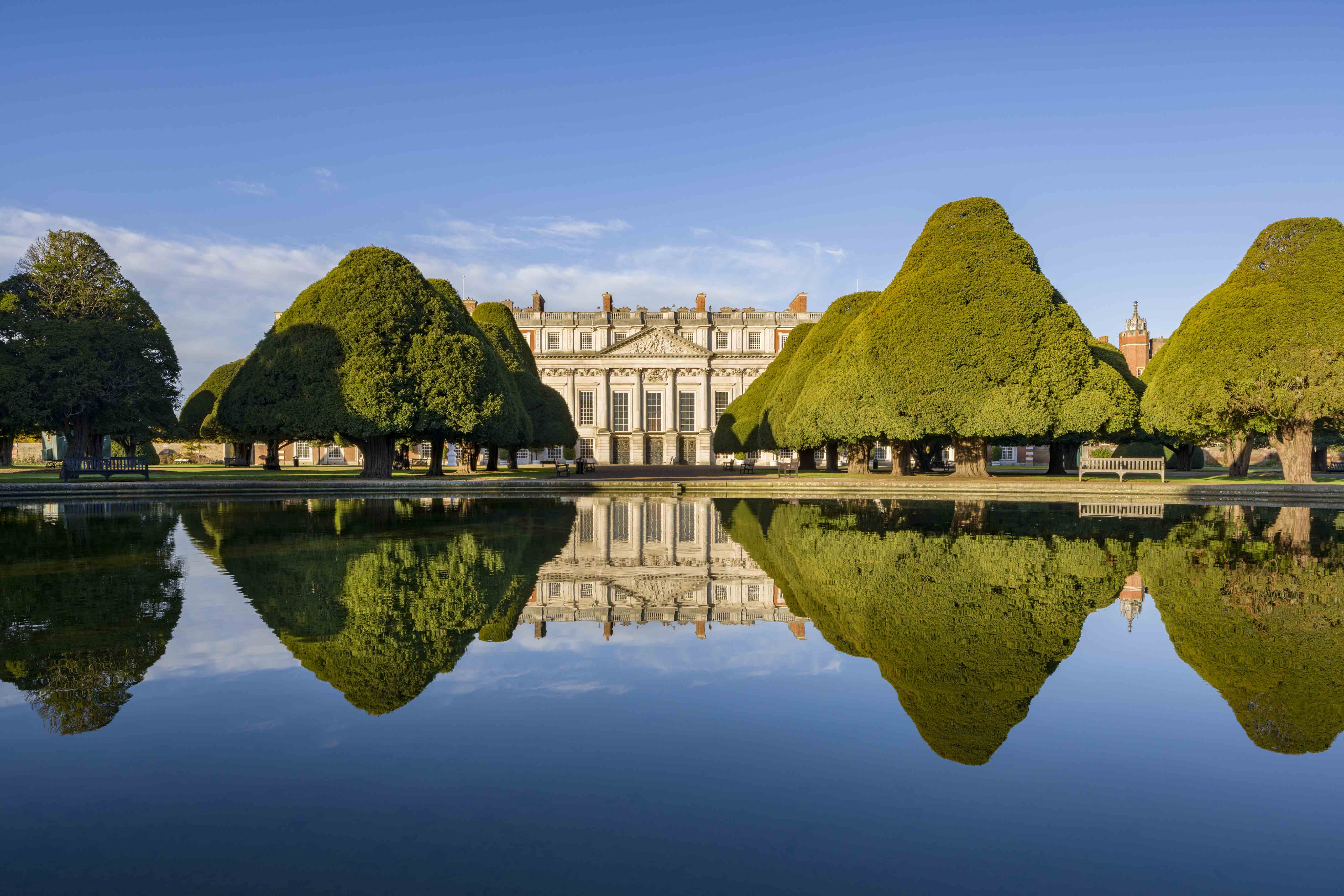Stately home reflected in a calm pond with trees and clear blue sky. Historic Royal Palaces, Chelsea flower show, Boodles garden.
