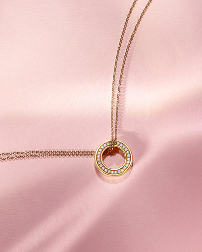Boodles gold Roulette necklace with a circular diamond charm on a pink satin background