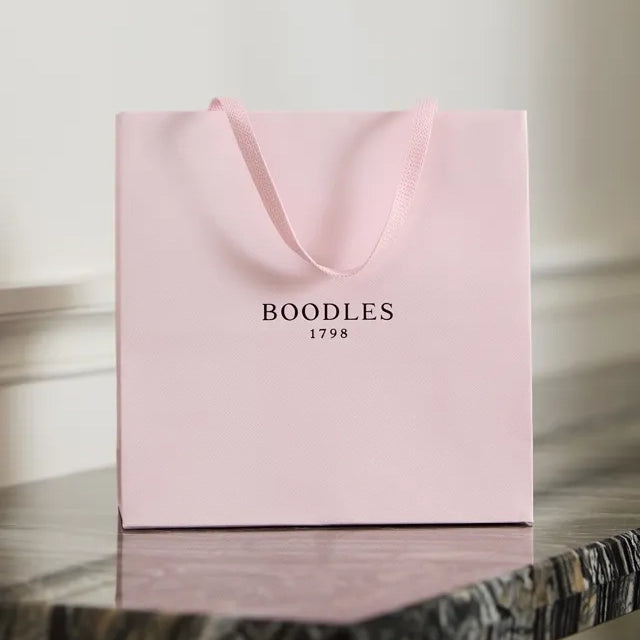 Signature pale pink Boodles luxury gift bag with ribbon handles resting on a marble surface.