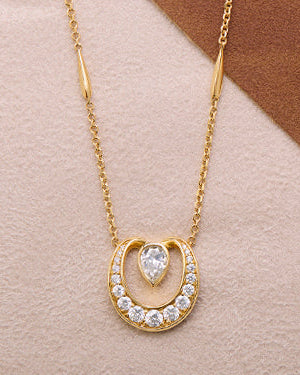 Boodles Lucky gold necklace with horse shoe shaped pendant set with diamonds on a brown and beige gradient background