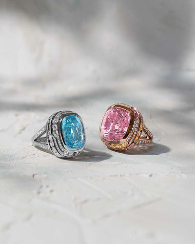 Two high jewellery rings in platinum and rose gold with large blue and pink gemstones made by Boodles on a light background